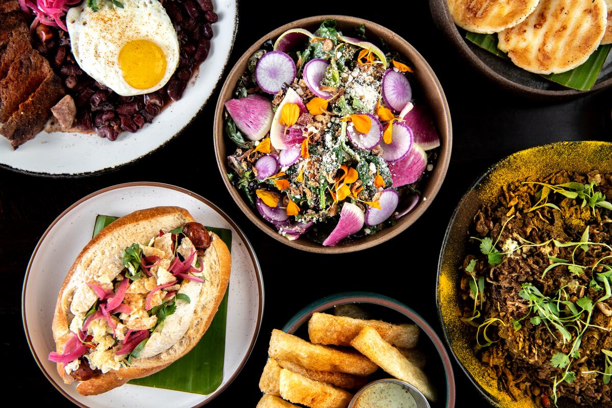 LONG BEACH, CA - JUNE 10: An array oof dishes from Selva, clockwise from top left: Bandeja paisa,market green salad, corn arepa, arroz chaufa, yucca fries and Colombian hot dog on Friday, June 10, 2022 in Long Beach, CA. (Mariah Tauger / Los Angeles Times)