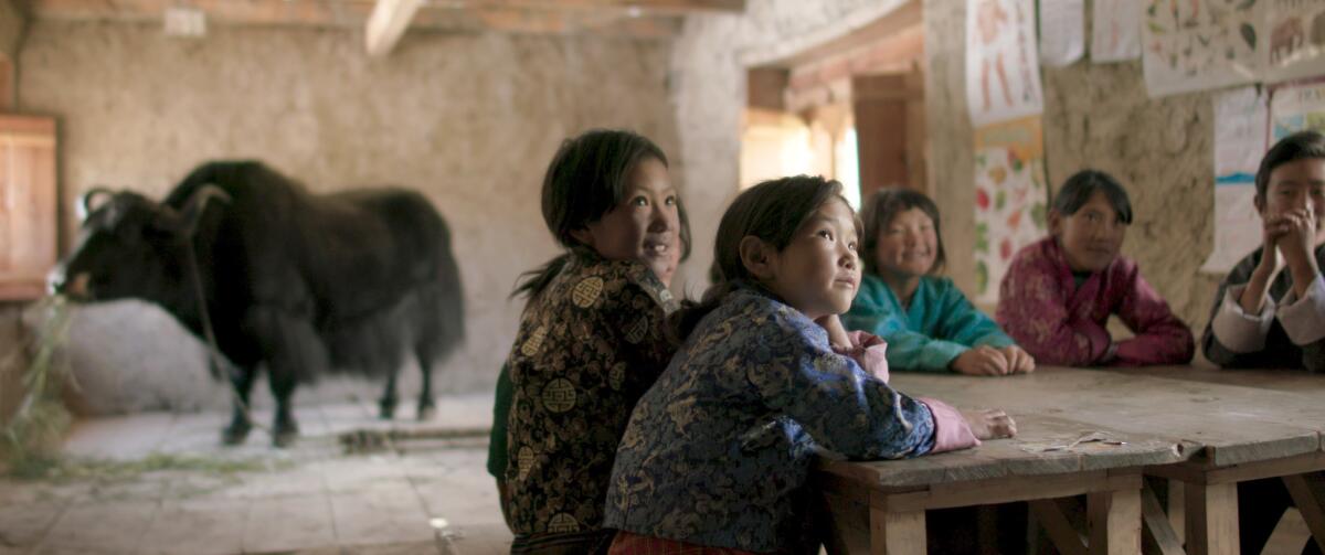 Young children sit at a table and a yak stands in the background.