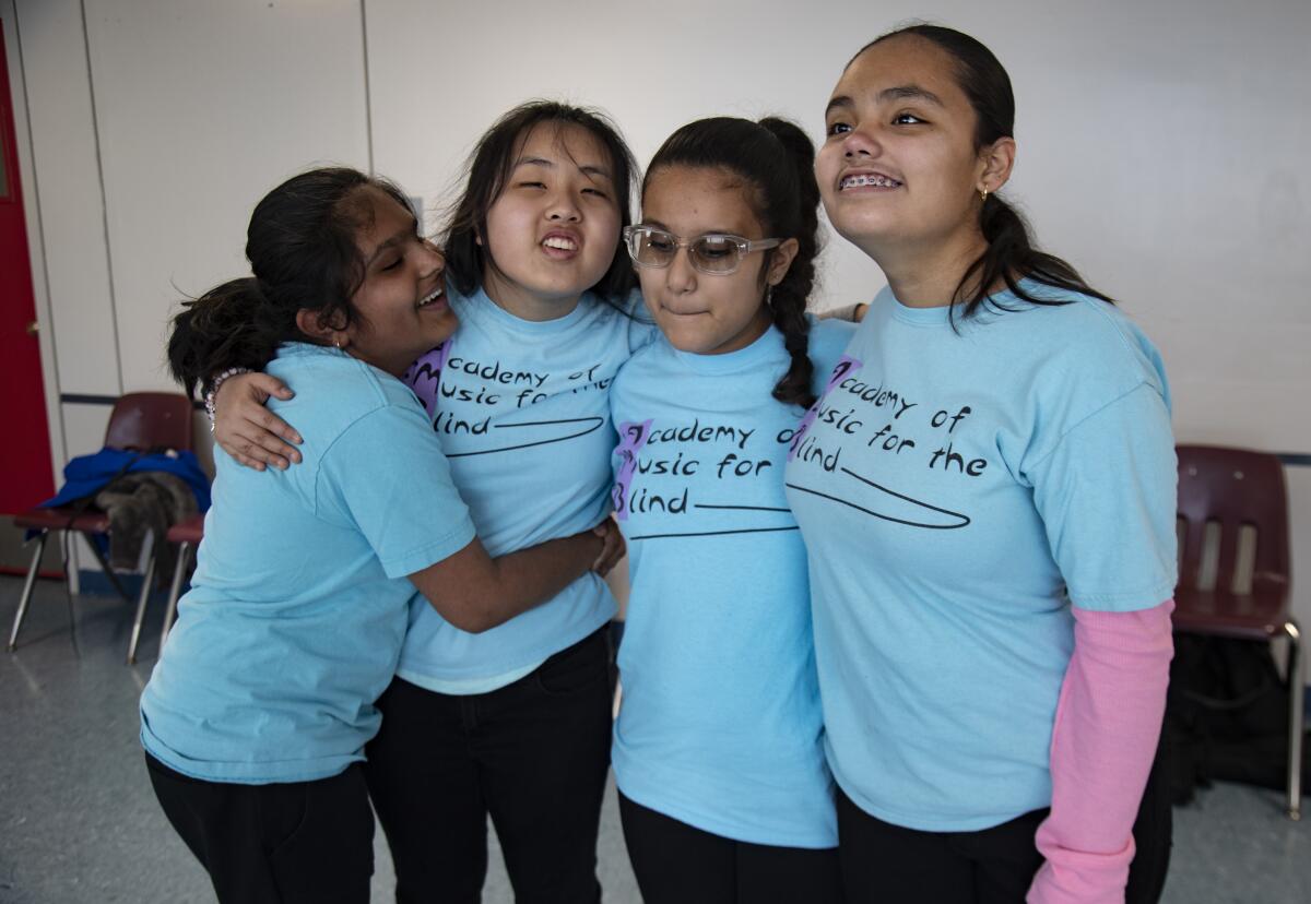 Four girls in a row with their arms around each other, all wearing blue Academy of Music for the Blind T-shirts.