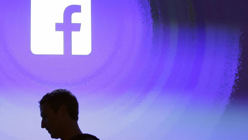 Facebook CEO Mark Zuckerberg is silhouetted beneath the company's logo.