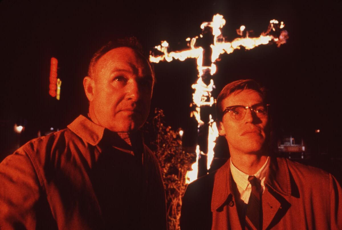 A night scene from "Mississippi Burning" shows two men looking into the distance with a burning cross behind them.