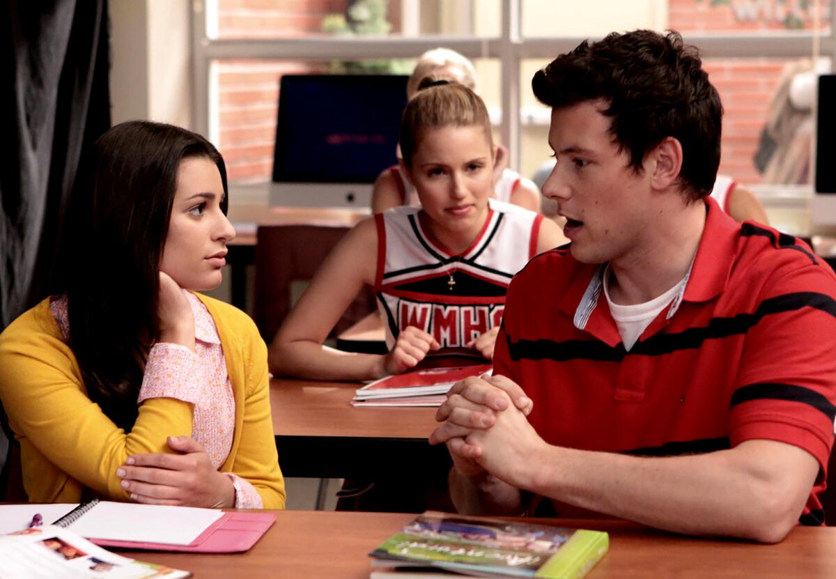 A girl and a boy talk, with a girl in the background looking on 