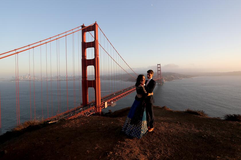SAN FRANCISCO CA - OCT. 22, 2020. Newlyweds Tulika Jha and Mike Borden take in the sunset at an overlook beside the Golden Gate Bridge in San Francisco on Thursday, Aug. 22, 2020. San Francisco has done an excellent job following public health guidance and made a huge leap from the coronavirus orange tier to the less restrictive yellow tier, providing a pathway for more businesses and activities to reopen. (Luis Sinco / Los Angeles Times)