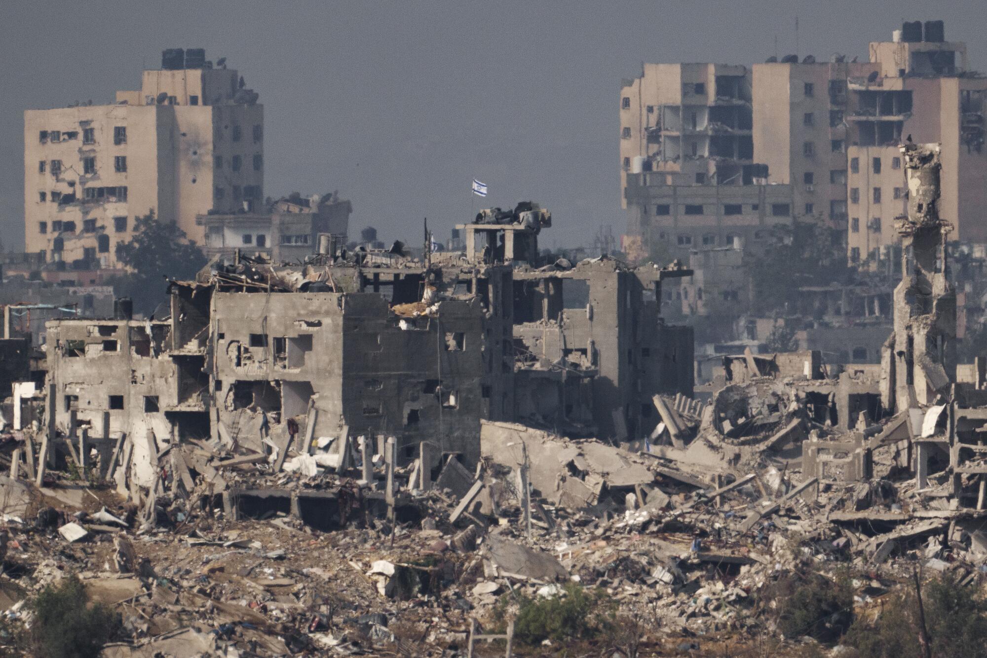 A flag flying in the distance atop a destroyed building surrounded by the ruins of other buildings 