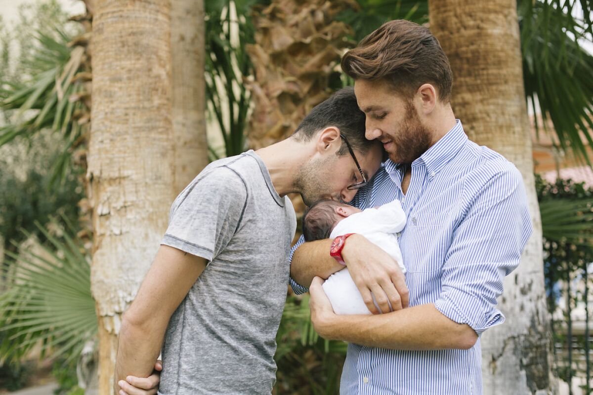 A man cradles a baby as his husband kisses the child's forehead in the documentary "Ghosts of the République."