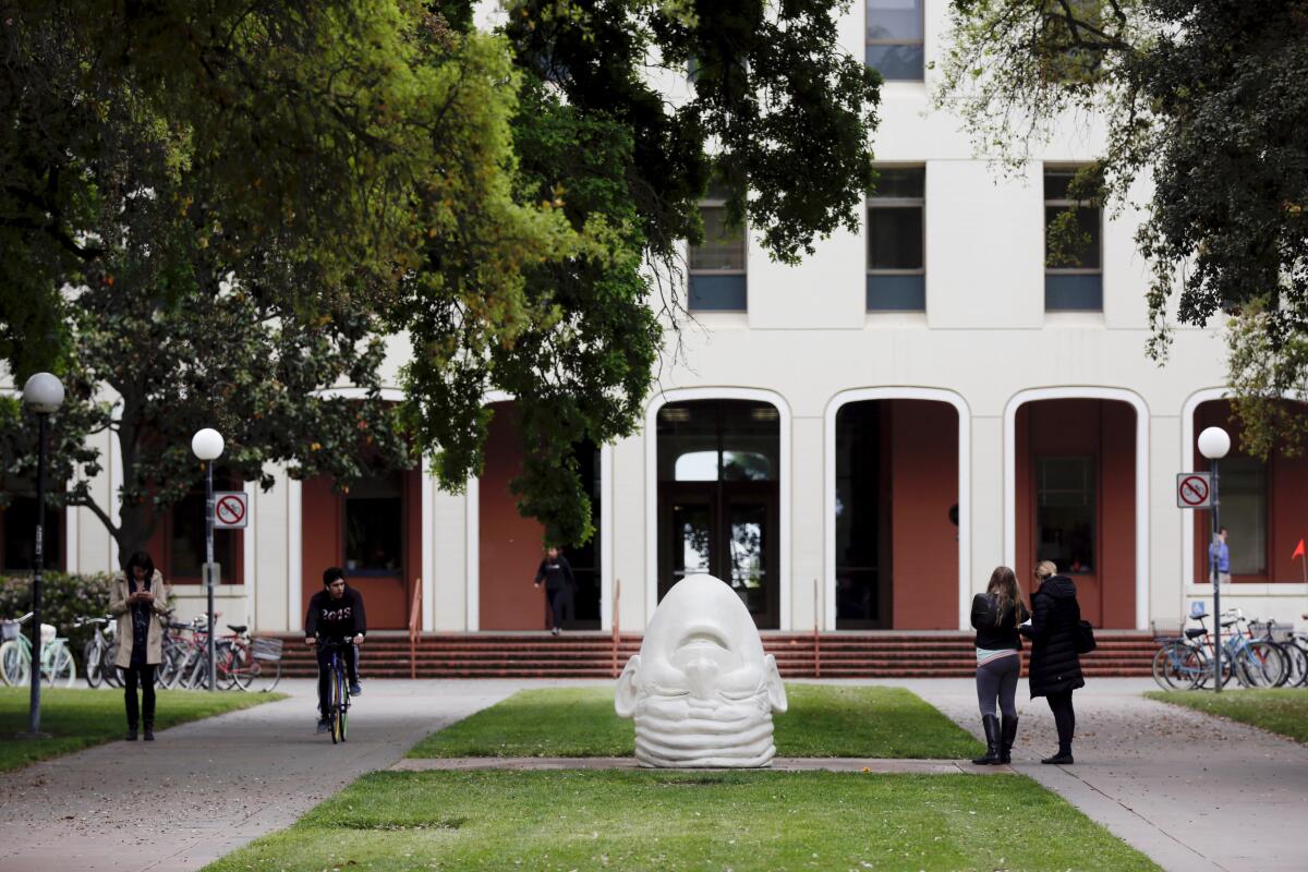 A few people outside a large white building near a white sculpture of an upside-down head