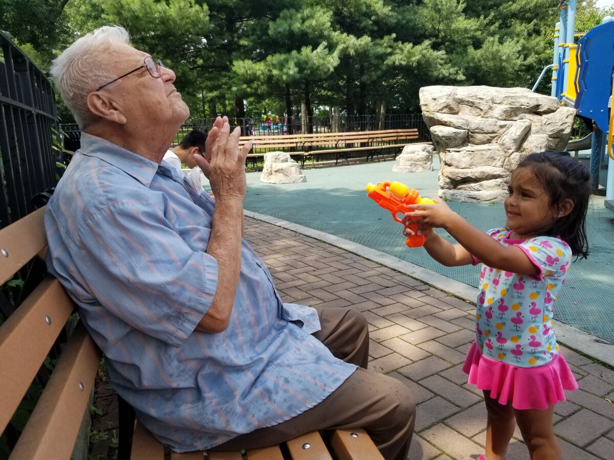 A man with gray hair holds up his hands as a young girl squirts him with a water gun.