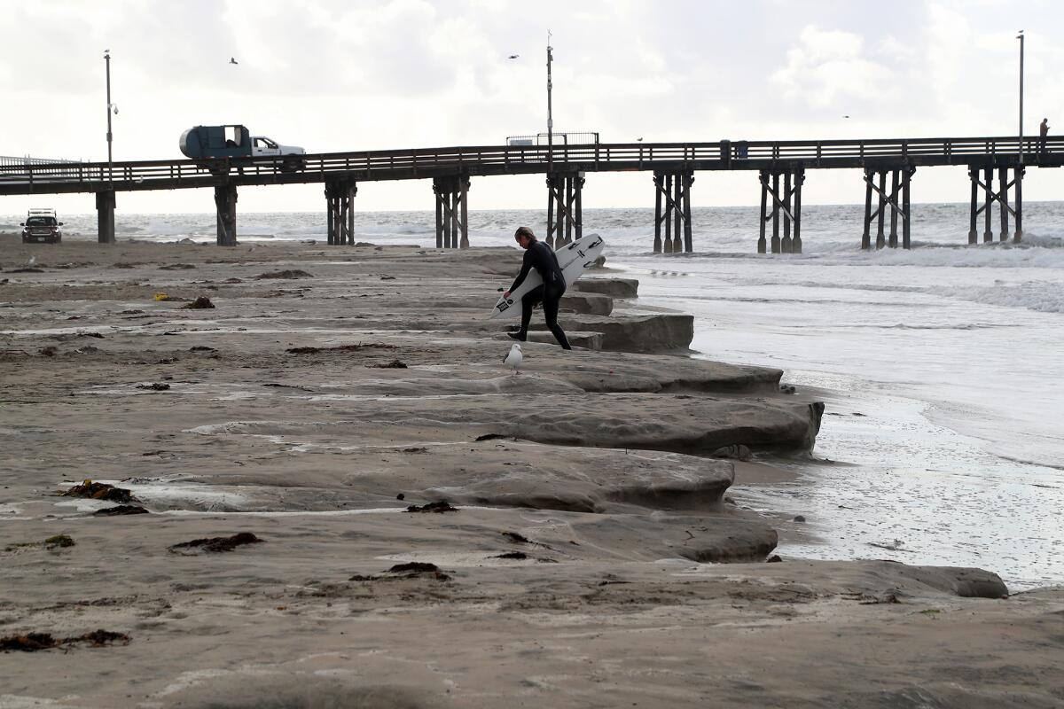A surfer steps onto the beach eroded by high tide along the north side of Newport Beach Pier on Friday.