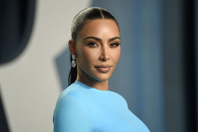 A woman with slicked back hair poses for the camera in a light blue dress