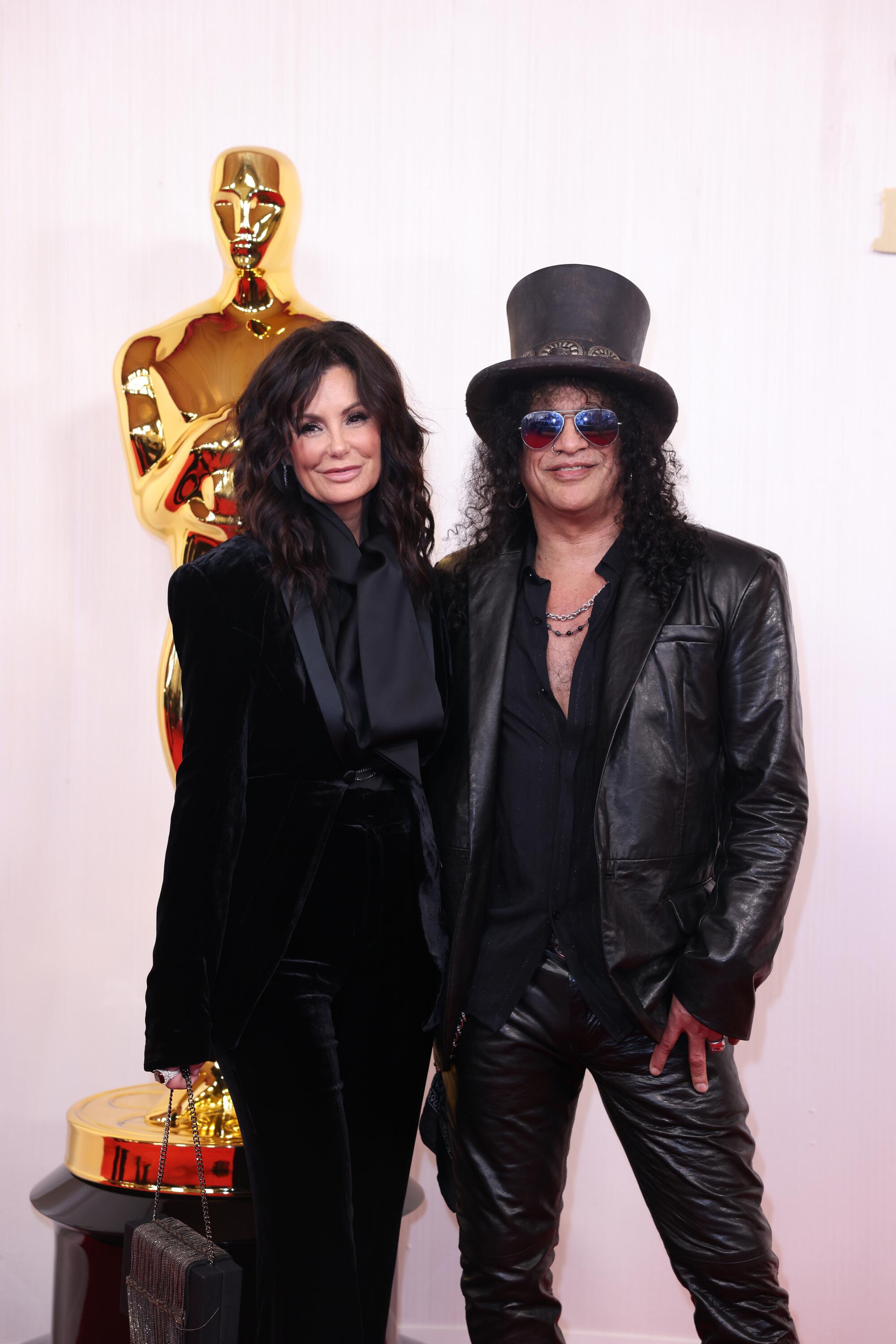 Meegan Hodges and Slash, both in black, pose in front of an Oscar statue. 