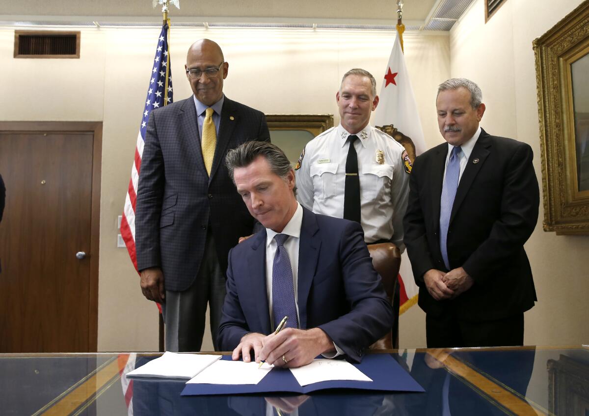Gov. Gavin Newsom signs a measure aimed at stabilizing the state's electric utilities in the face of devastating wildfires caused by their equipment, as the bill's author, Assemblyman Chris Holden, D-Pasadena, left, Thom Porter, the director for the California Department of Forestry and Fire Protection, center, and Mark Ghilarducci, the director of the California Governor's Office Emergency Services, right, look on in Sacramento.
