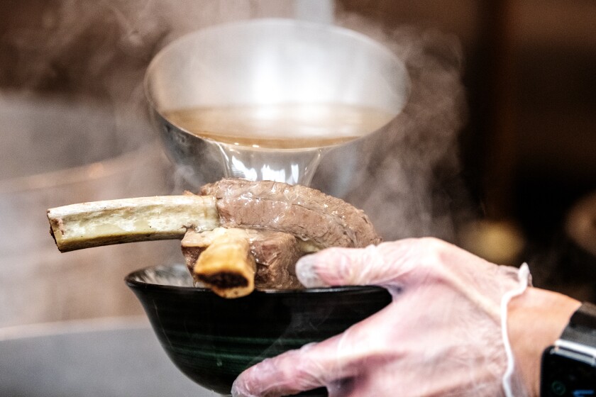 Chef Viet Nguyen ladles pho broth onto braised rib bones.