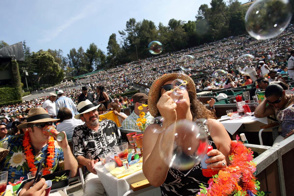 A woman wearing a hat and sunglasses blows bubbles in the crowd at the Hollywood Bowl during a concert.