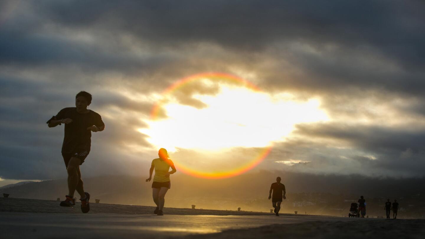 Joggers and cyclists use on bike path along Santa Monica beach at sunset.