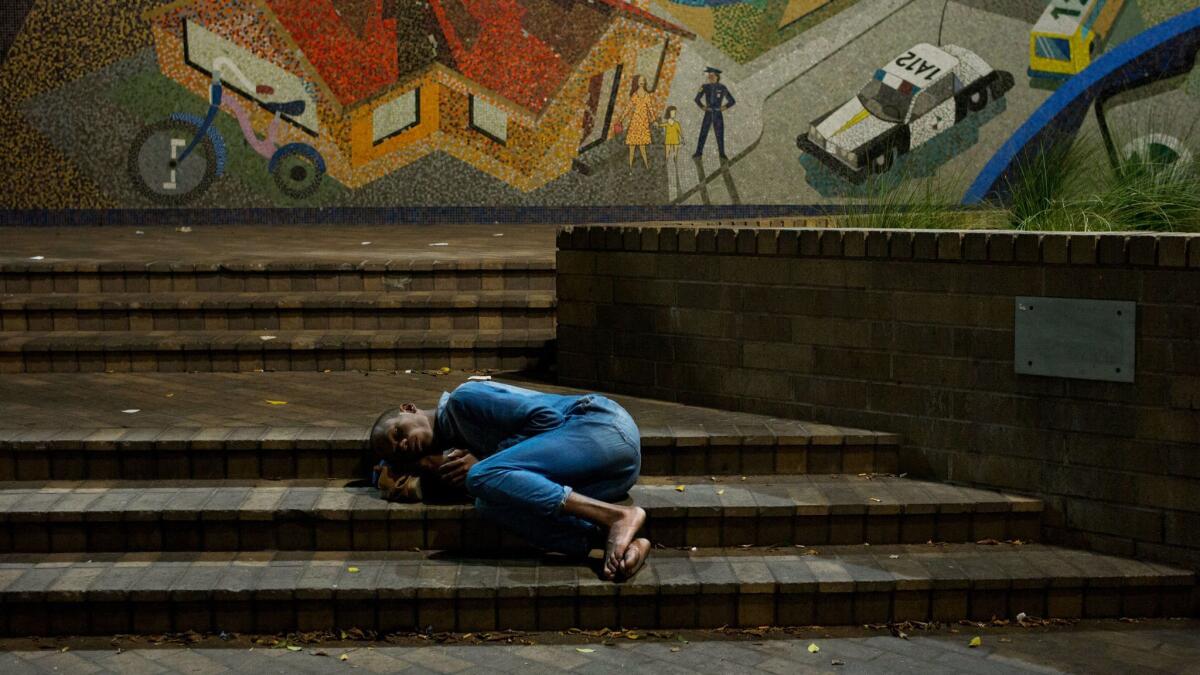 A homeless man sleeps on the steps of the LAPD station on skid row in September.