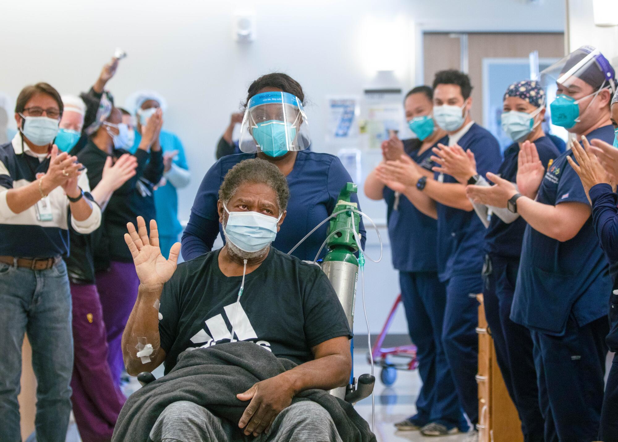 Perry waves from his wheelchair as hospital staff applaud on either side of a hallway.