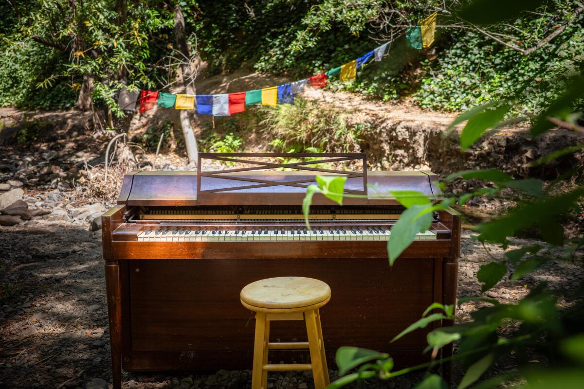 An upright piano with a stool is seen outdoors.