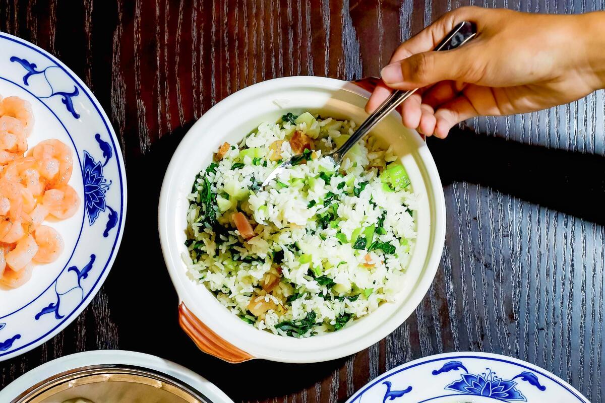 A bowl containing a rice and greens dish, with a plate of shrimp to one side.