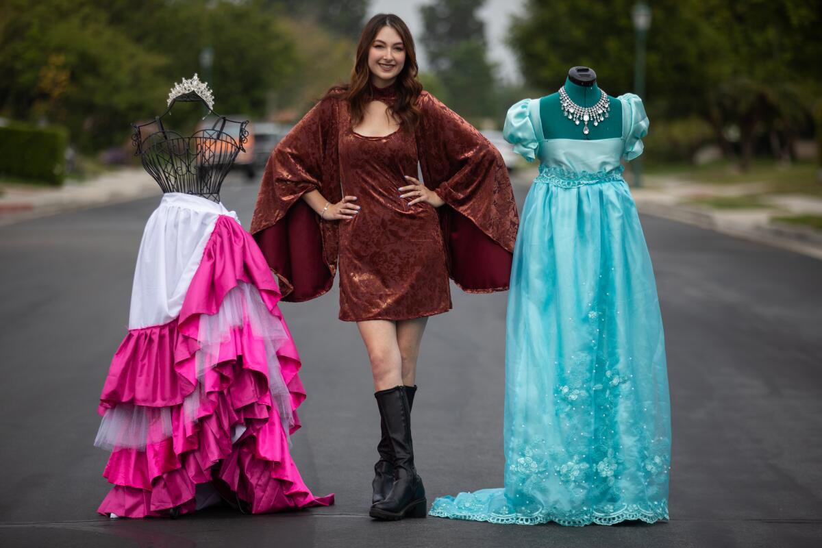 A young woman in a dress next to two other dresses on mannequins