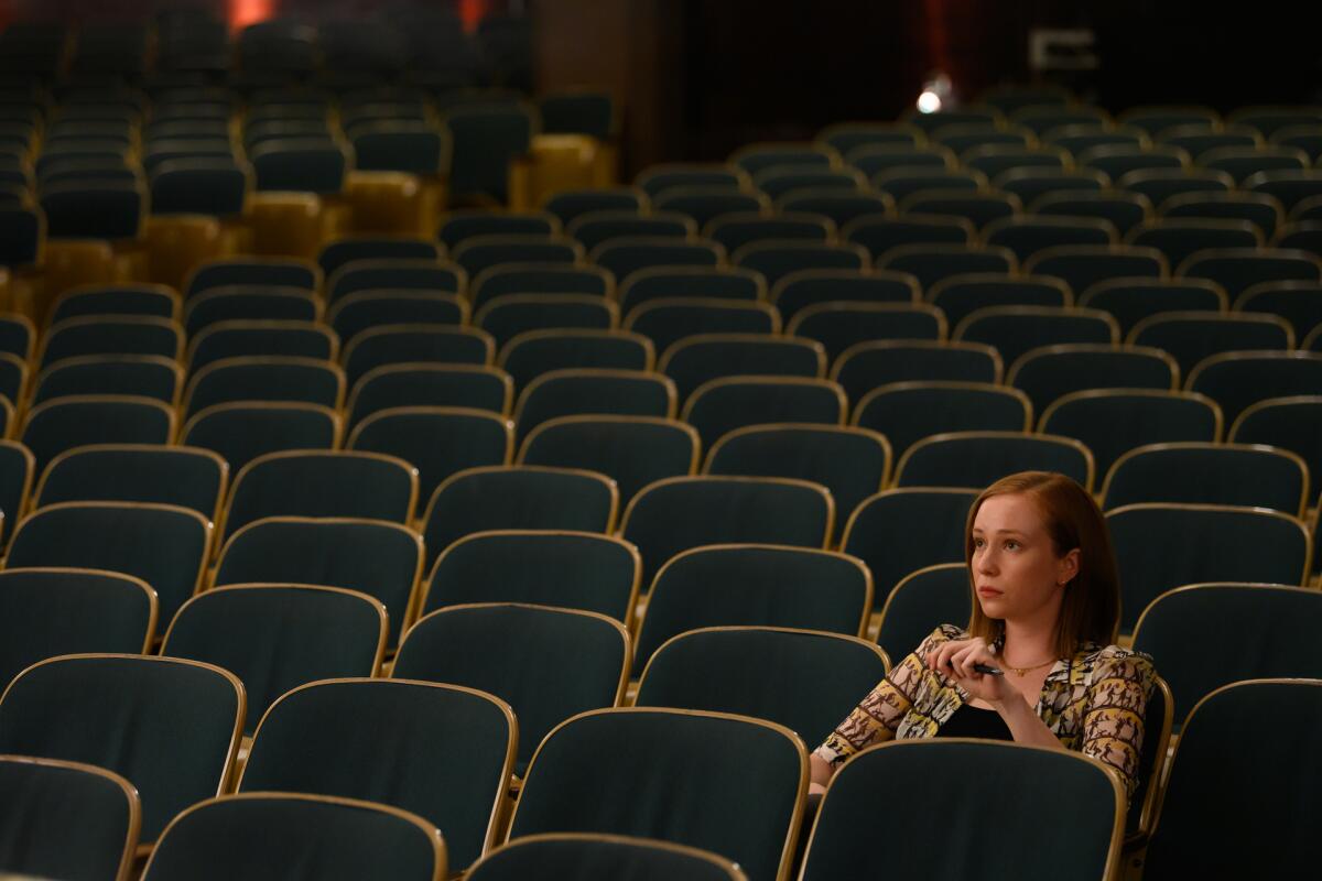 A woman sits in a seat in an empty auditorium.