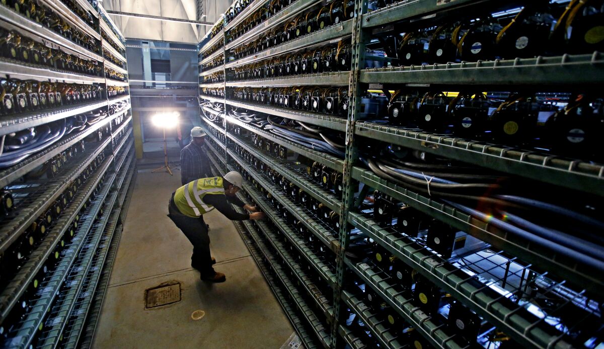 Workers look over racks of Bitcoin data miners.