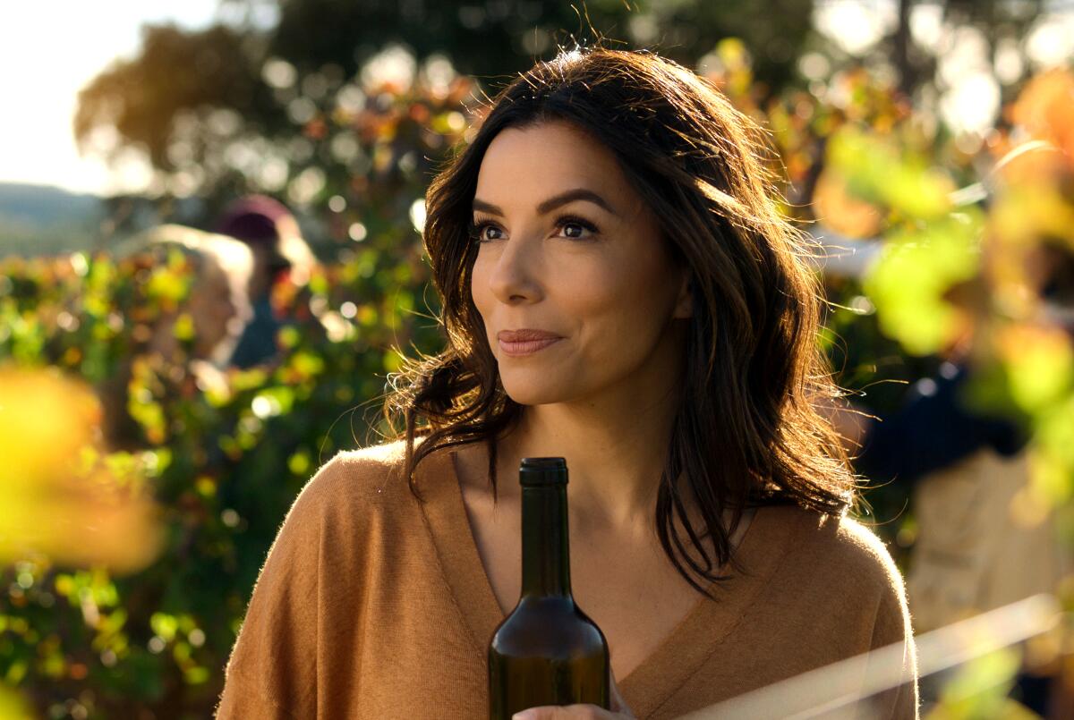 A woman standing in a vineyard hold a bottle of wine.