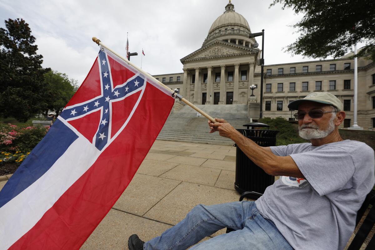 A man waves the current Mississippi state flag as he sits in front of the Capitol.