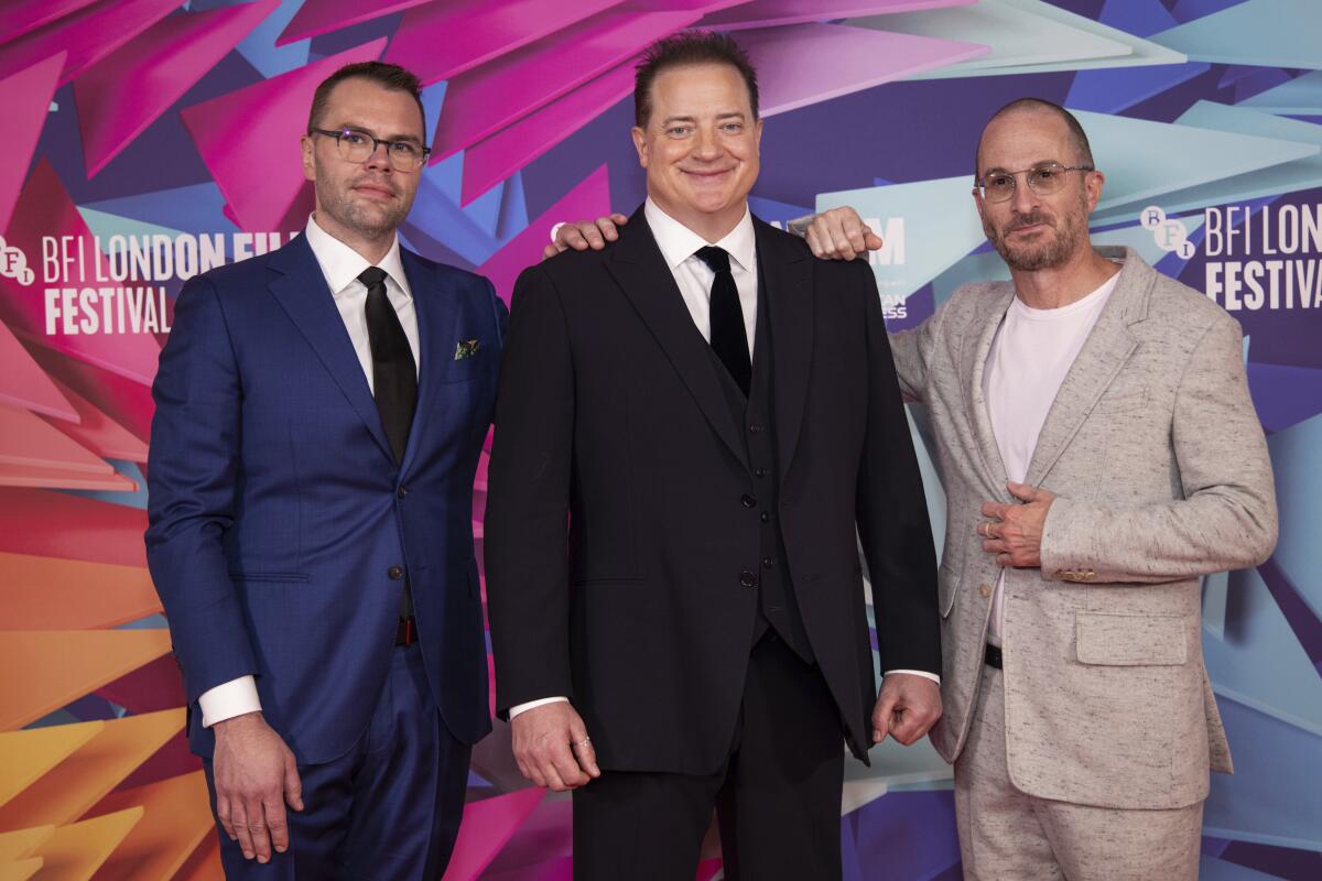 Three men wearing suits and smiling pose in front of a film festival backdrop.