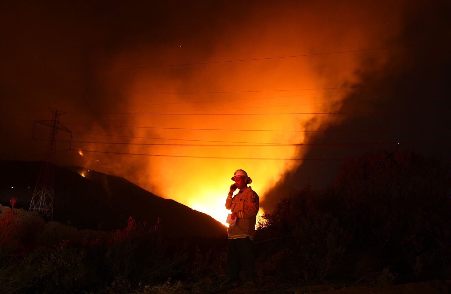 Nathan Judy, a U.S. Forest Service fire information officer, talks on a satellite phone as flames from the Powerhouse fire burn along San Francisquito Canyon Road in the Angeles National Forest.