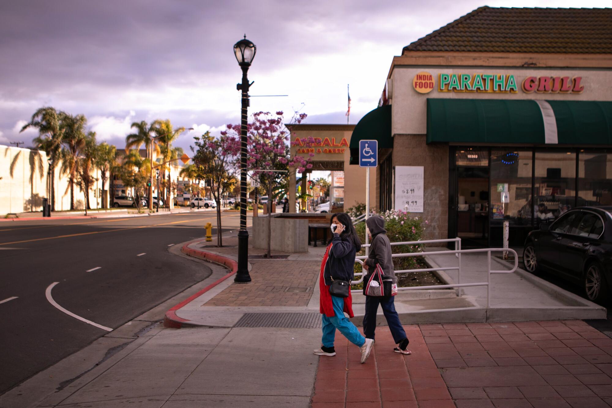 Two people walk in a shopping district in front of a restaurant 
