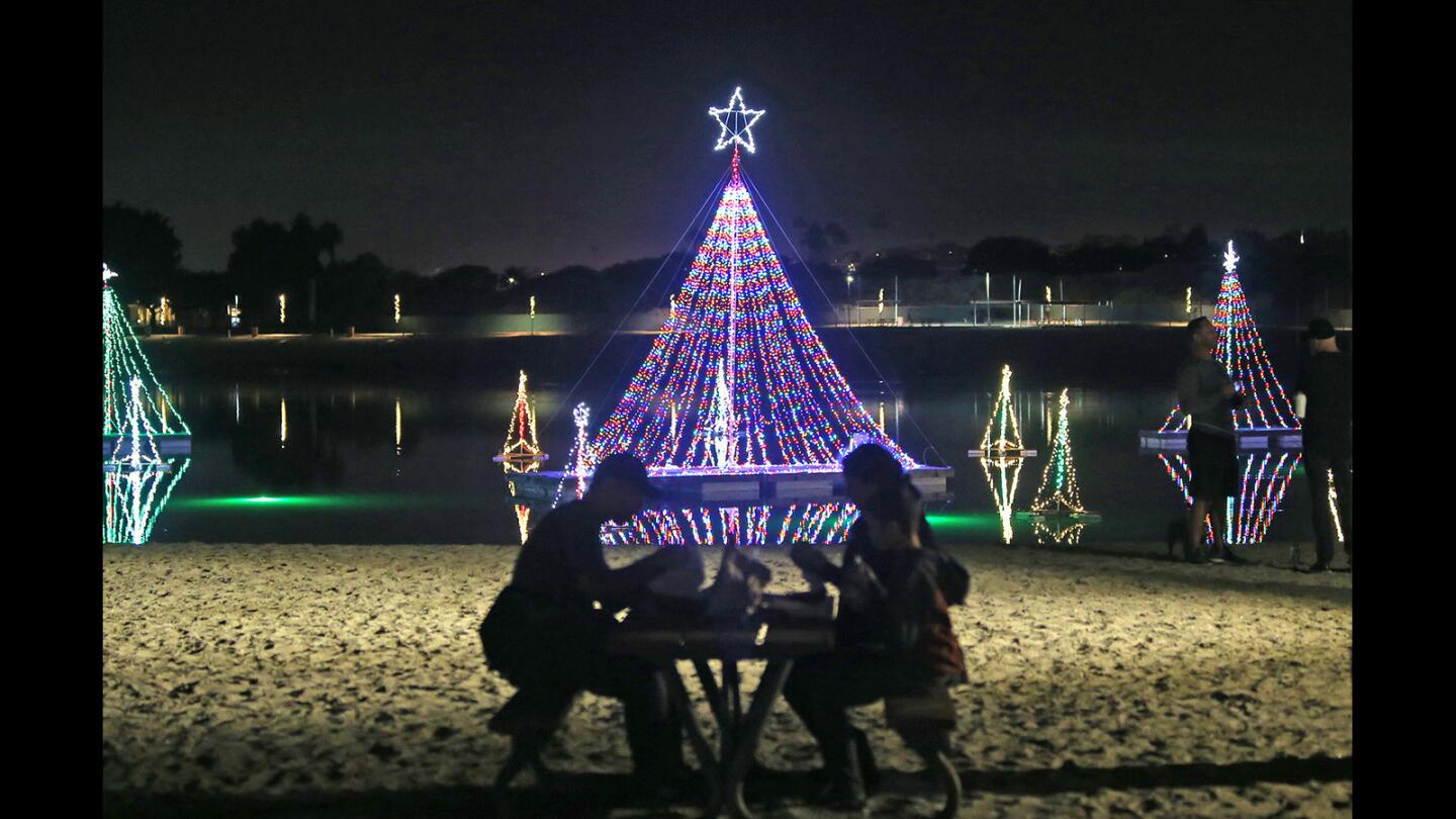 With a backdrop of tree-shaped lights on the Back Bay, guests eat hamburgers on the sand during the 27th annual Lighting of the Bay holiday celebration Friday at Newport Dunes Waterfront Resort in Newport Beach.