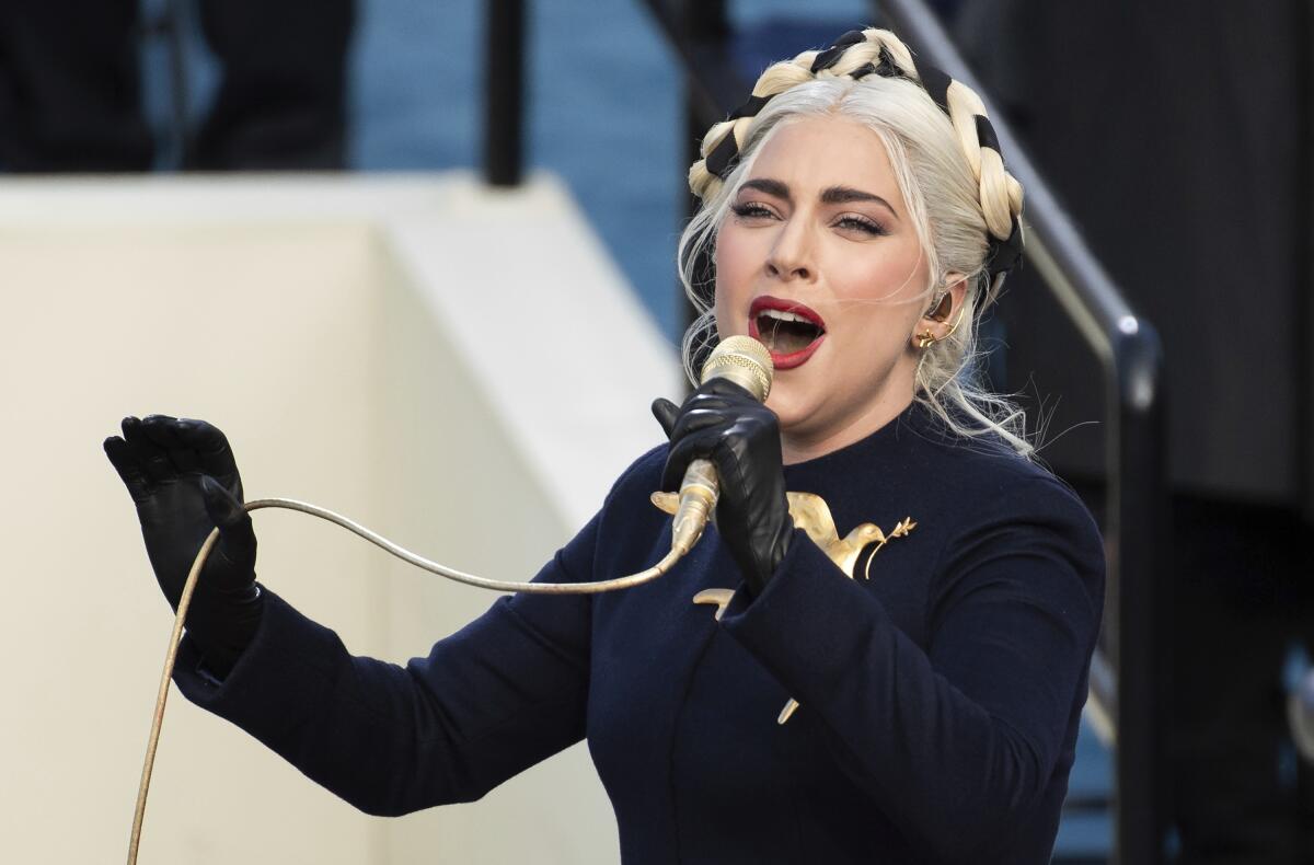 A blond woman in a dark coat sings into a microphone