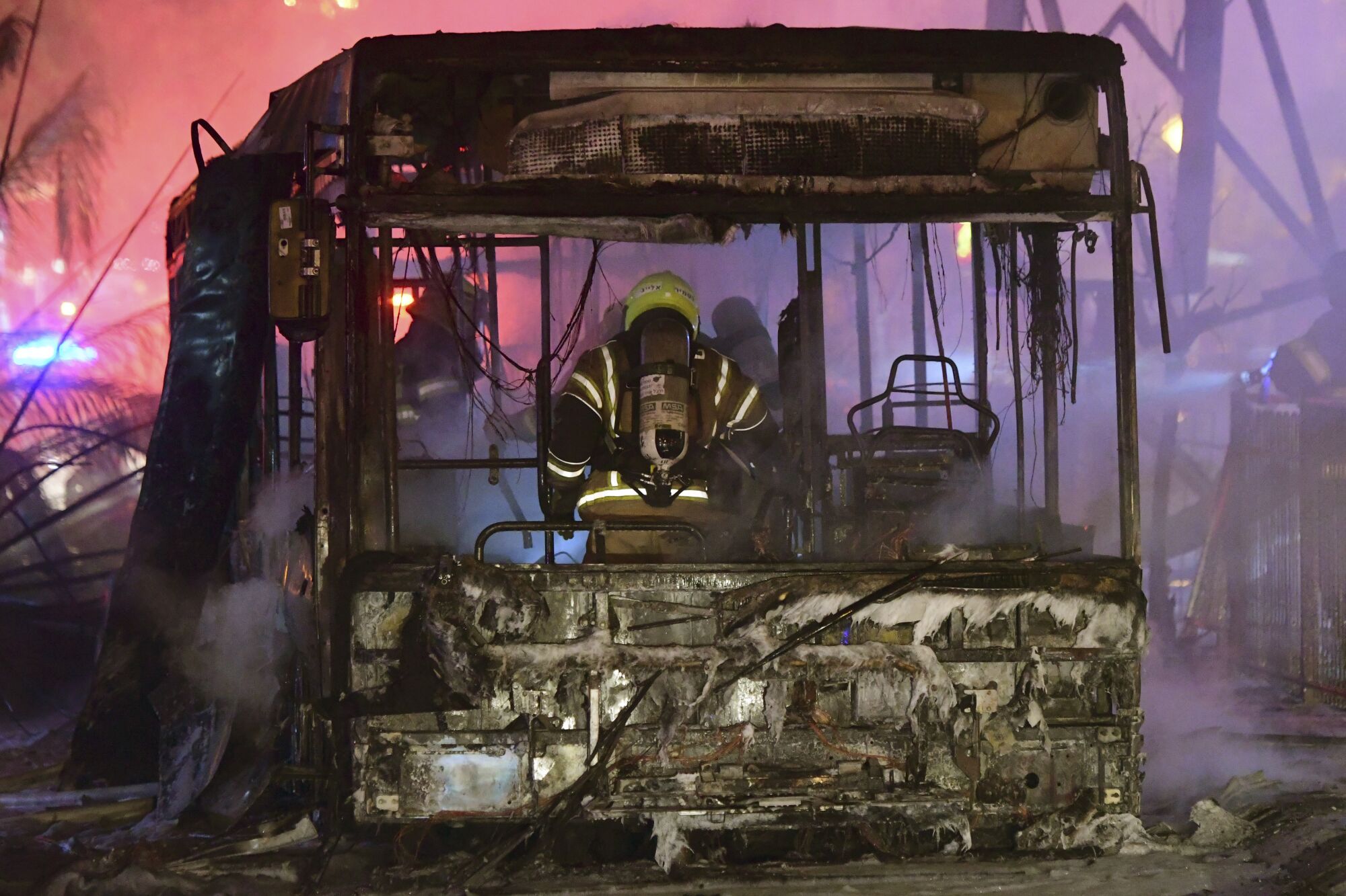 A  firefighter stand in the scorched wreckage of a bus 