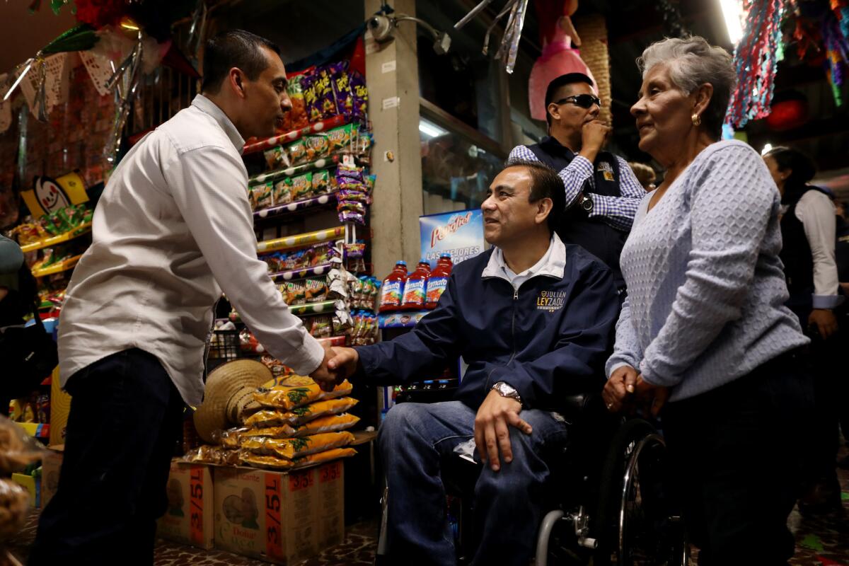 Julián Leyzaola se encuentra con los empresarios Gilberto Estrada, a la izquierda, y su madre, Elodia Ramírez, mientras hace campaña en el Mercado Miguel Hidalgo en Tijuana. (Gary Coronado / Los Angeles Times)