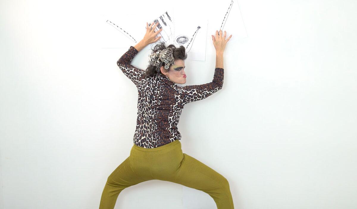 A woman in green pants against a white wall.