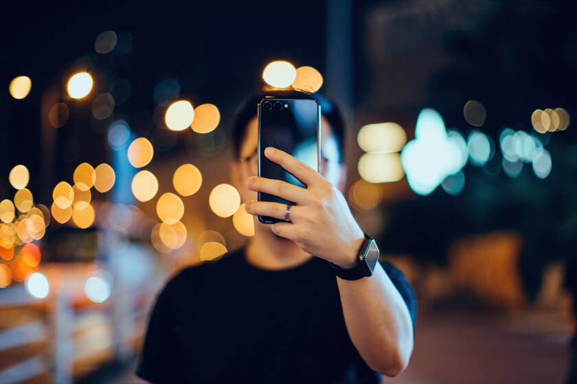 A young man snaps a selfie with his smartphone on a city street.