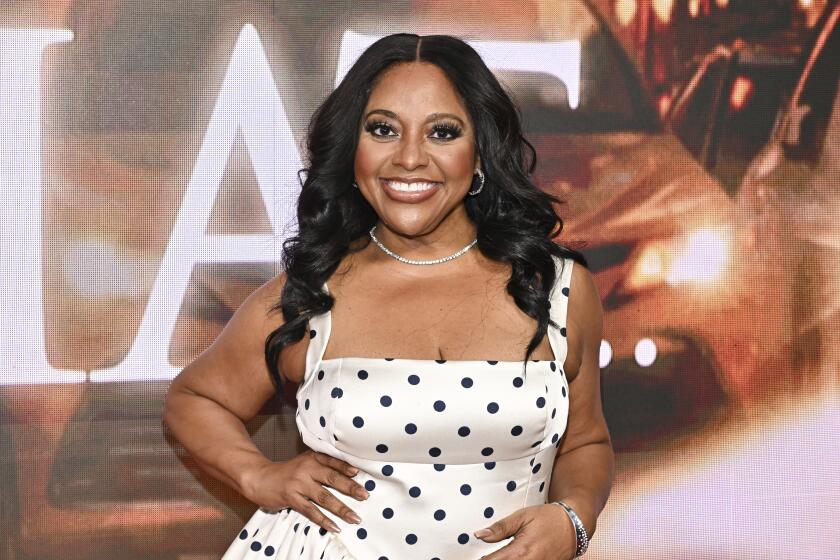 Sherri Shepherd in a white polka‑dot dress posing with her hands on her hips at a red carpet.
