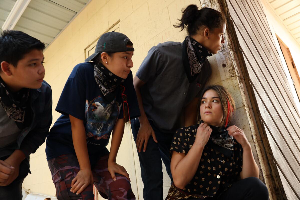 Four teens peer around the corner of a building