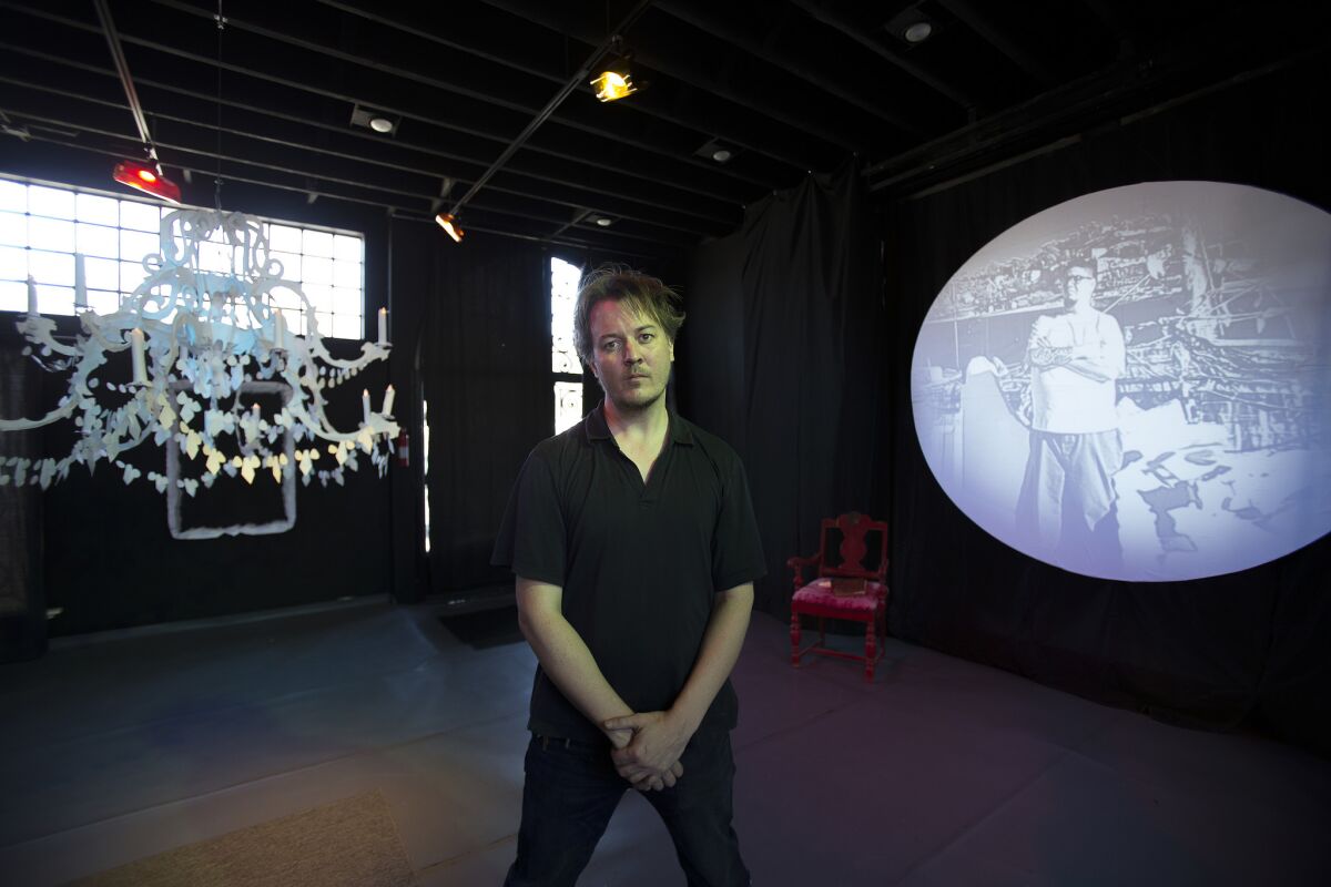 Jim Ovelmen stands inside AWOL gallery, with pieces that evoke an old explorer's club. To the right, on the screen, is street artist Mondo Bobadilla, visible through the installation's periscope.