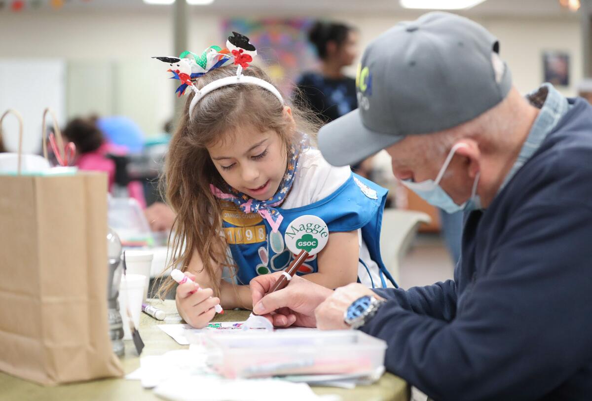 Maggie, a Girl Scout, colors a card with a senior at Adult Day Health Care Center.
