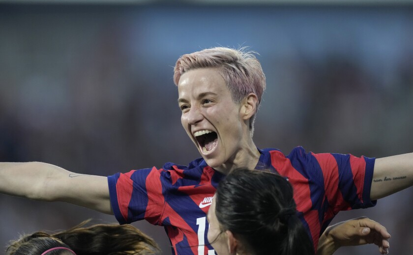 Megan Rapinoe throws her arms out and shouts in celebration with teammates.