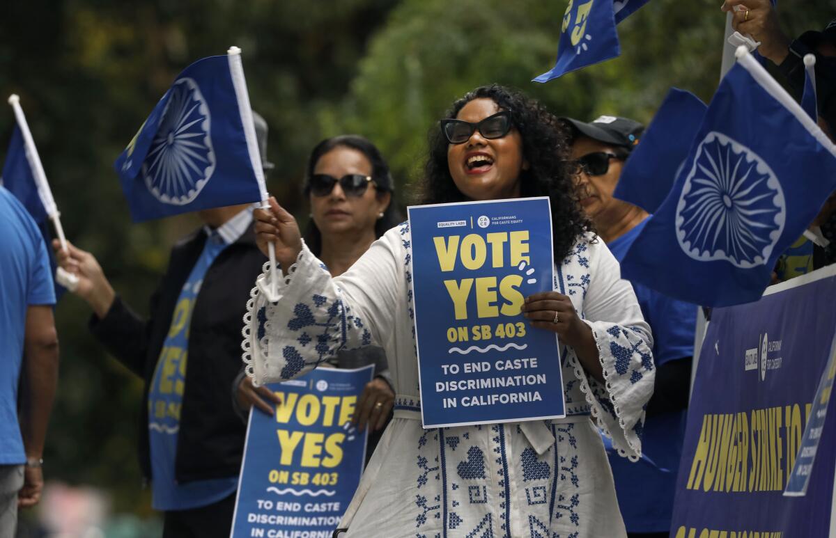 People wave blue-and-white flags and hold blue signs reading, "Vote yes on SB 403 to end caste discrimination in California."