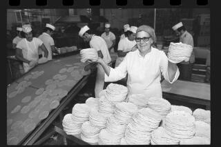 A woman holds stacks of tortillas at a tortilla factory.