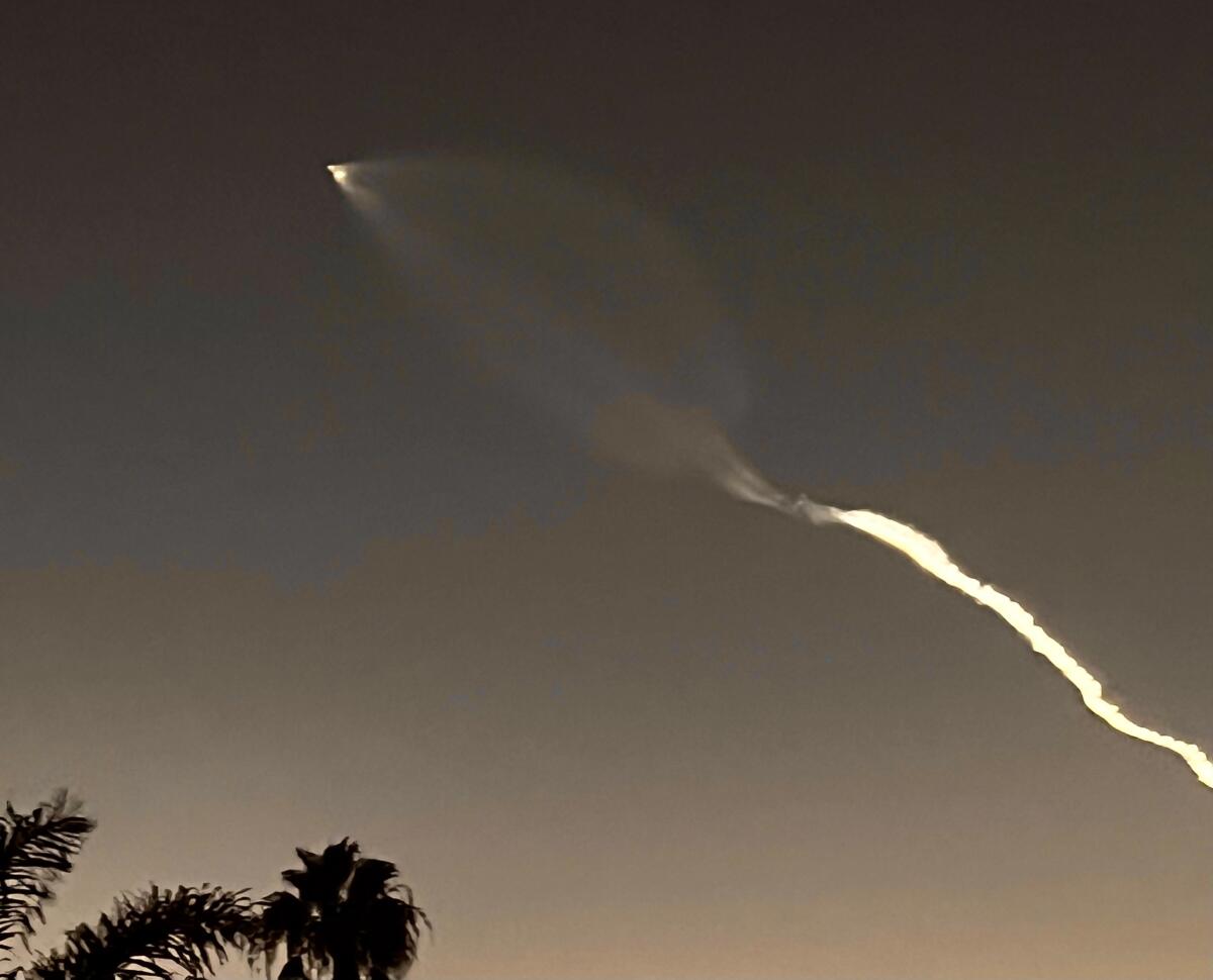 A rocket, seen as a bright speck, powers skyward leaving an exhaust trail behind.