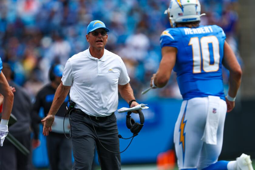 Chargers coach Jim Harbaugh meets Justin Herbert as he runs off the field against  the Carolina Panthers.