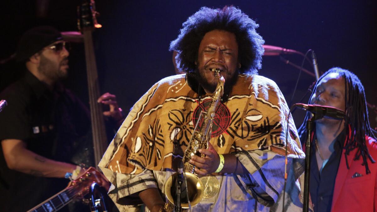 Kamasi Washington performs on his saxophone, surrounded by other musicians.