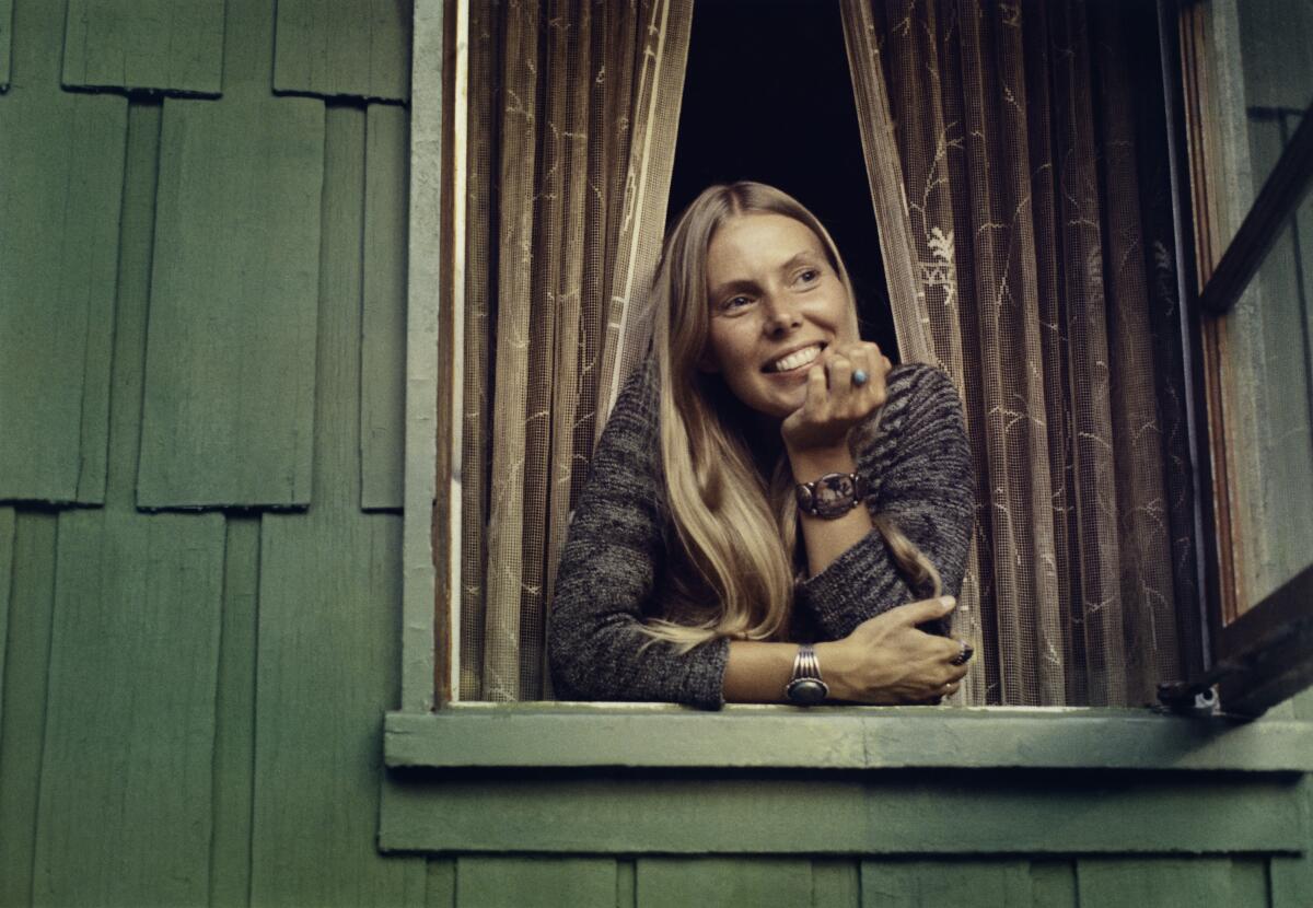 Joni Mitchell looks out a window, smiling