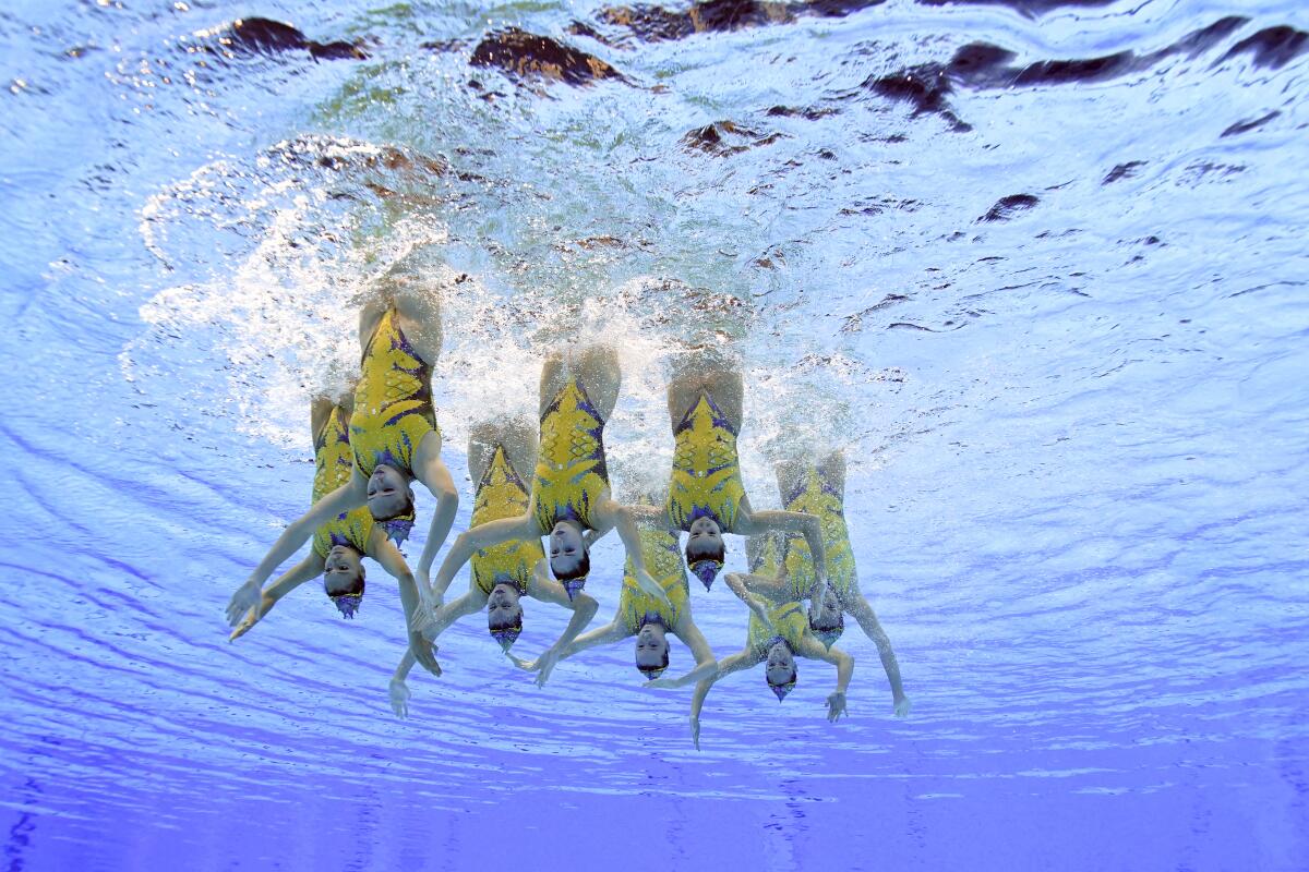 Underwater view of artistic swimmers holding a vertical position with their feet in the air