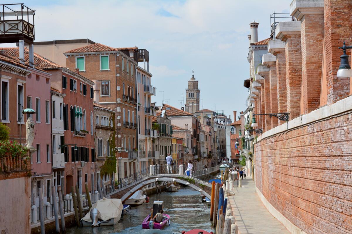 A man transports a refrigerator on a boat through a picturesque Venice canal.