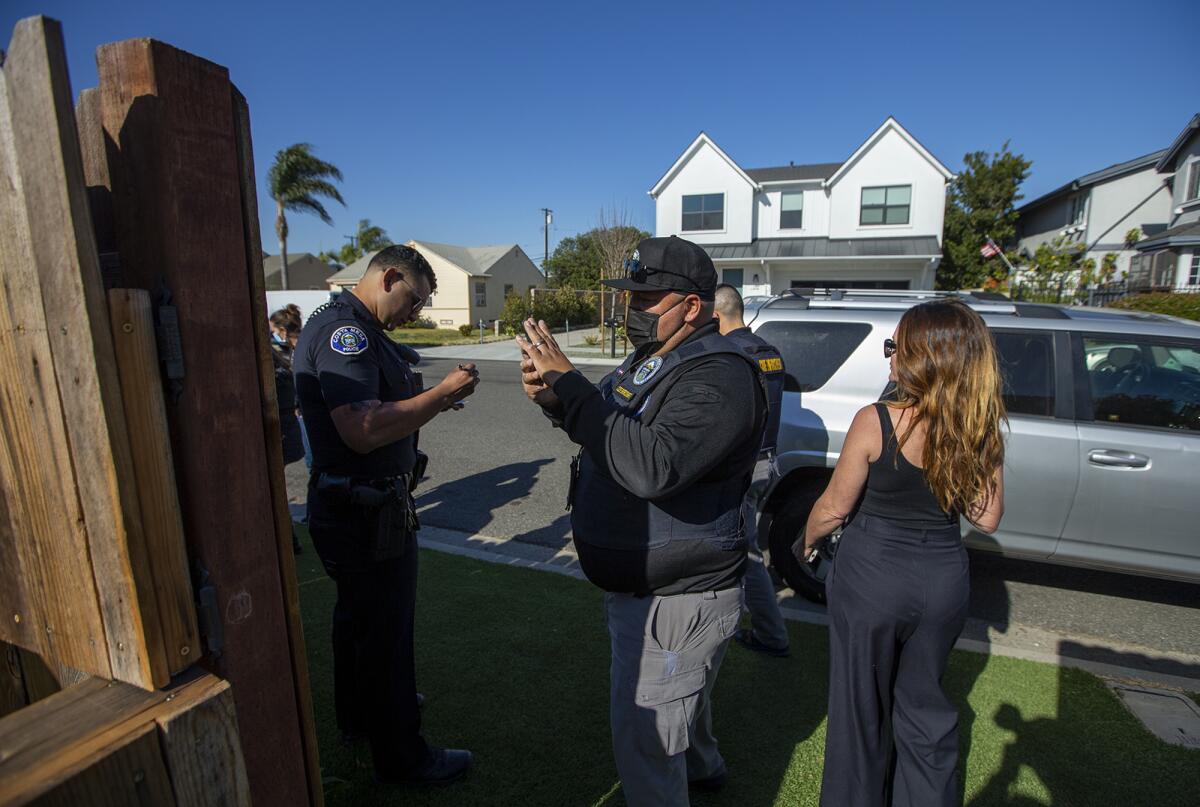A Costa Mesa code enforcement officer photographs the fence at Camp Lila as owner Katie Sherouse looks on Friday, March 11.
